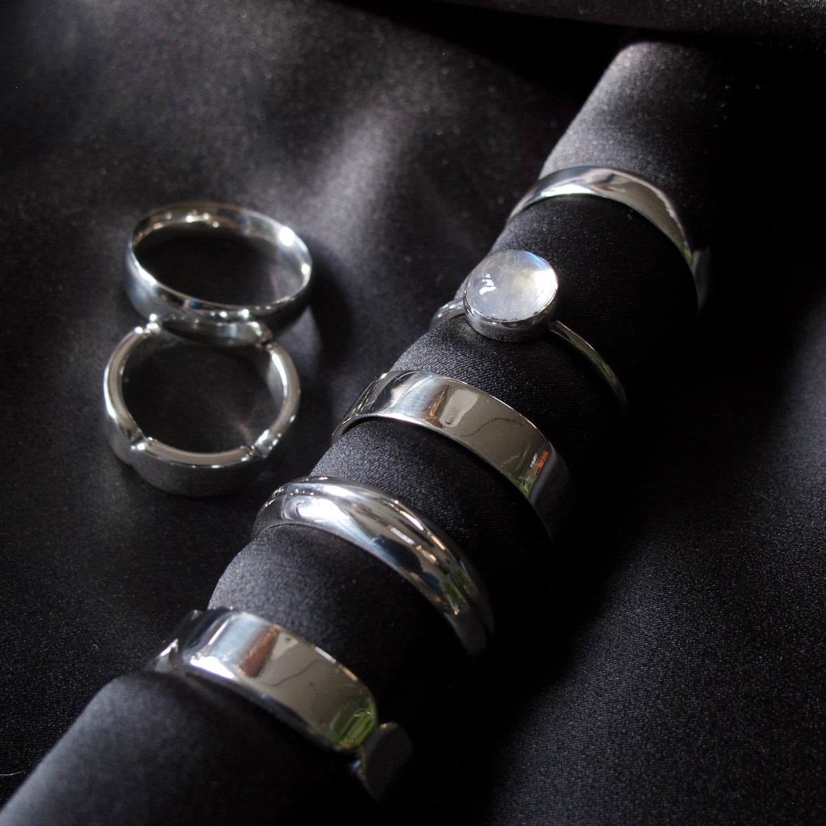 A set of polished silver rings displayed on a black velvet ring roll, with two additional rings placed beside it on a matching black fabric background.