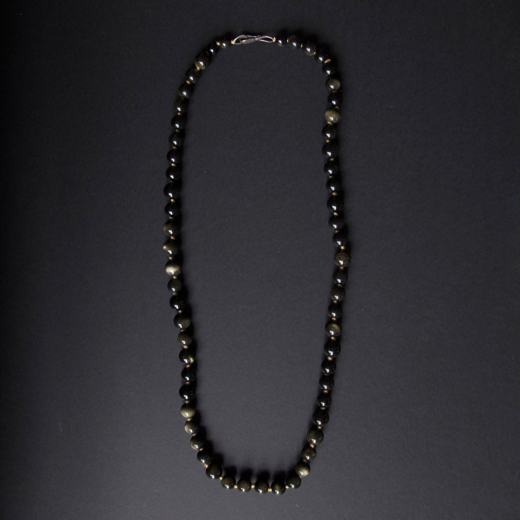 A beaded necklace composed of alternating black and metallic gold beads, arranged in a vertical loop on a dark gray background.
