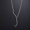 A delicate pearl necklace with a gold toggle clasp and ring connector, displayed on a dark textured background.