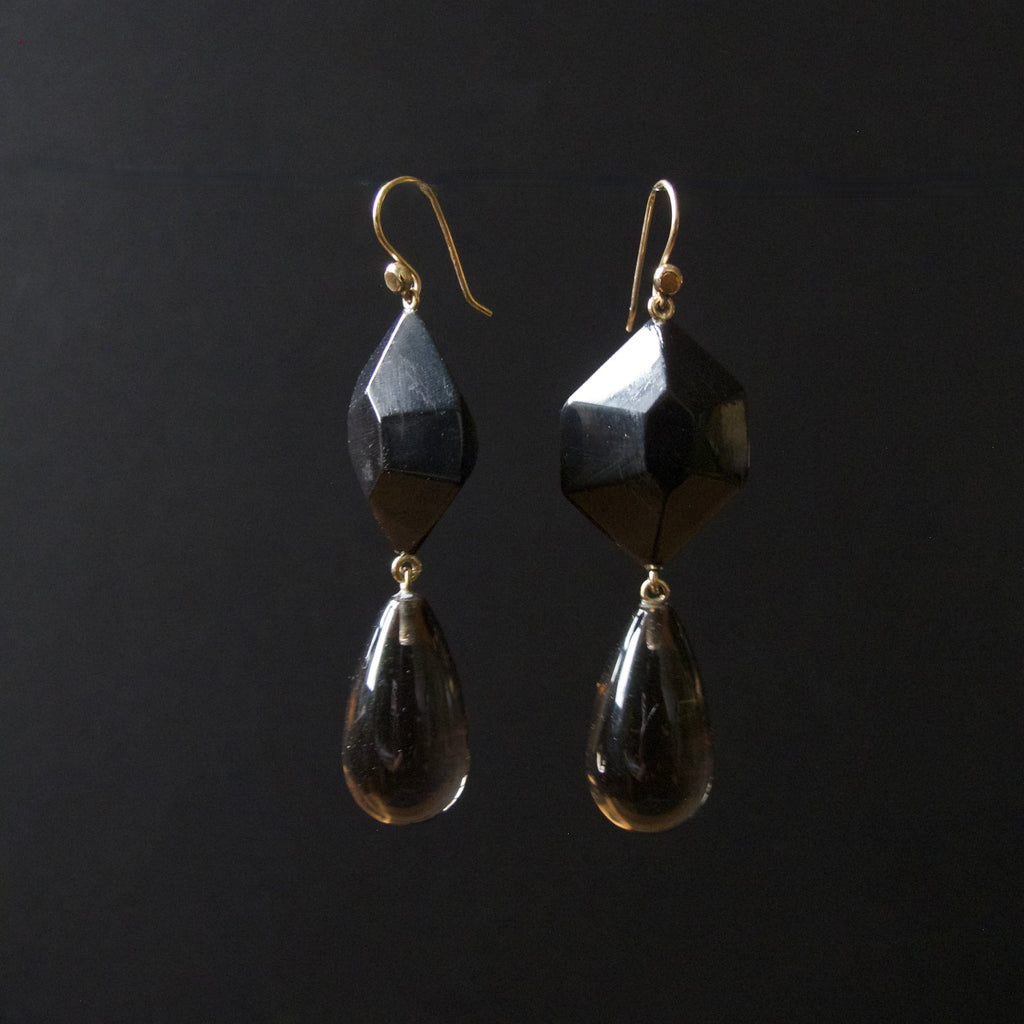 A pair of black faceted gemstone drop earrings with gold fishhook ear wires, displayed against a solid black background.