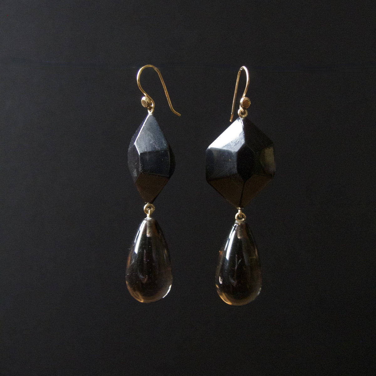 A pair of black faceted gemstone drop earrings with gold fishhook ear wires, displayed against a solid black background.
