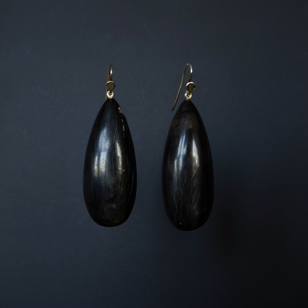 A pair of teardrop-shaped black wooden earrings with gold fishhook wires, displayed against a dark gray background.