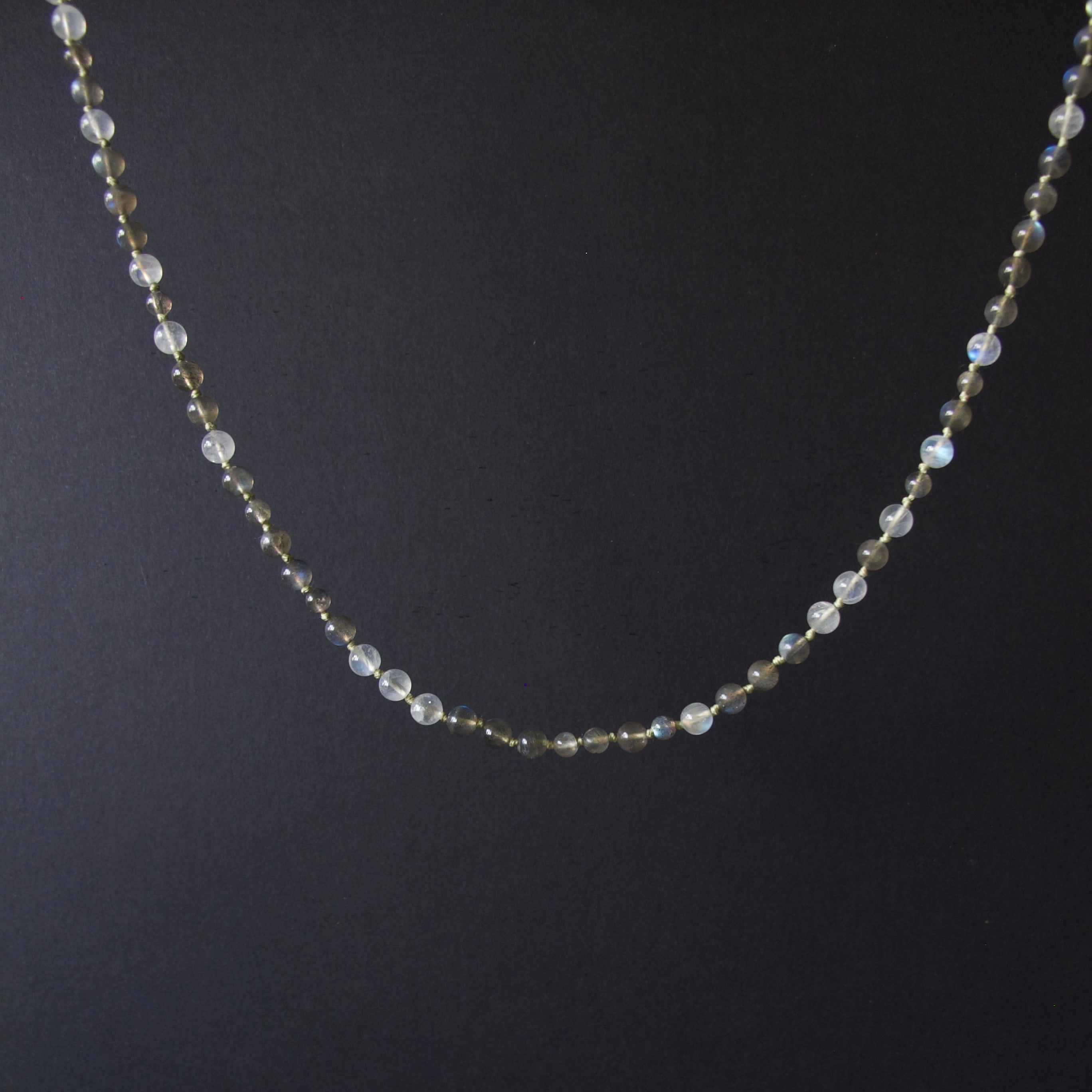 A delicate beaded necklace with small iridescent white beads and tiny gold spacer beads, displayed against a dark black background.