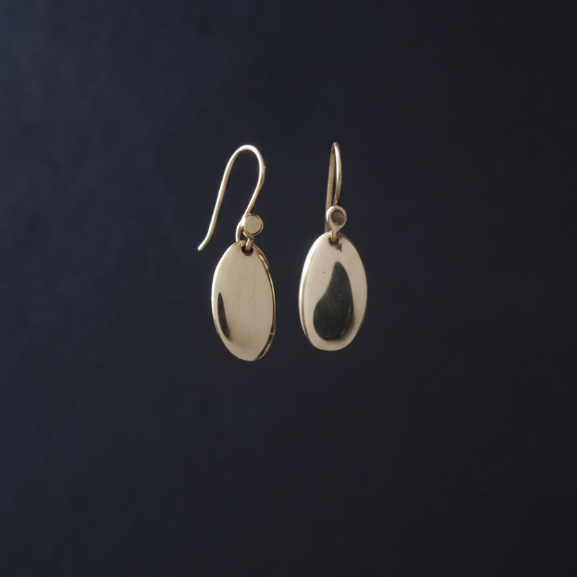 a pair of small smooth gold oval polished earrings against a dark background