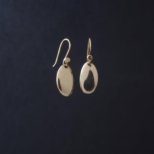 a pair of small smooth gold oval polished earrings against a dark background