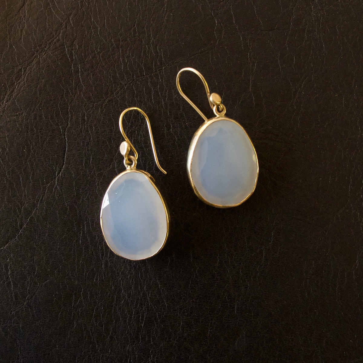 A pair of gold drop earrings with teardrop-shaped milky white cabochon stones, displayed on a textured black background.