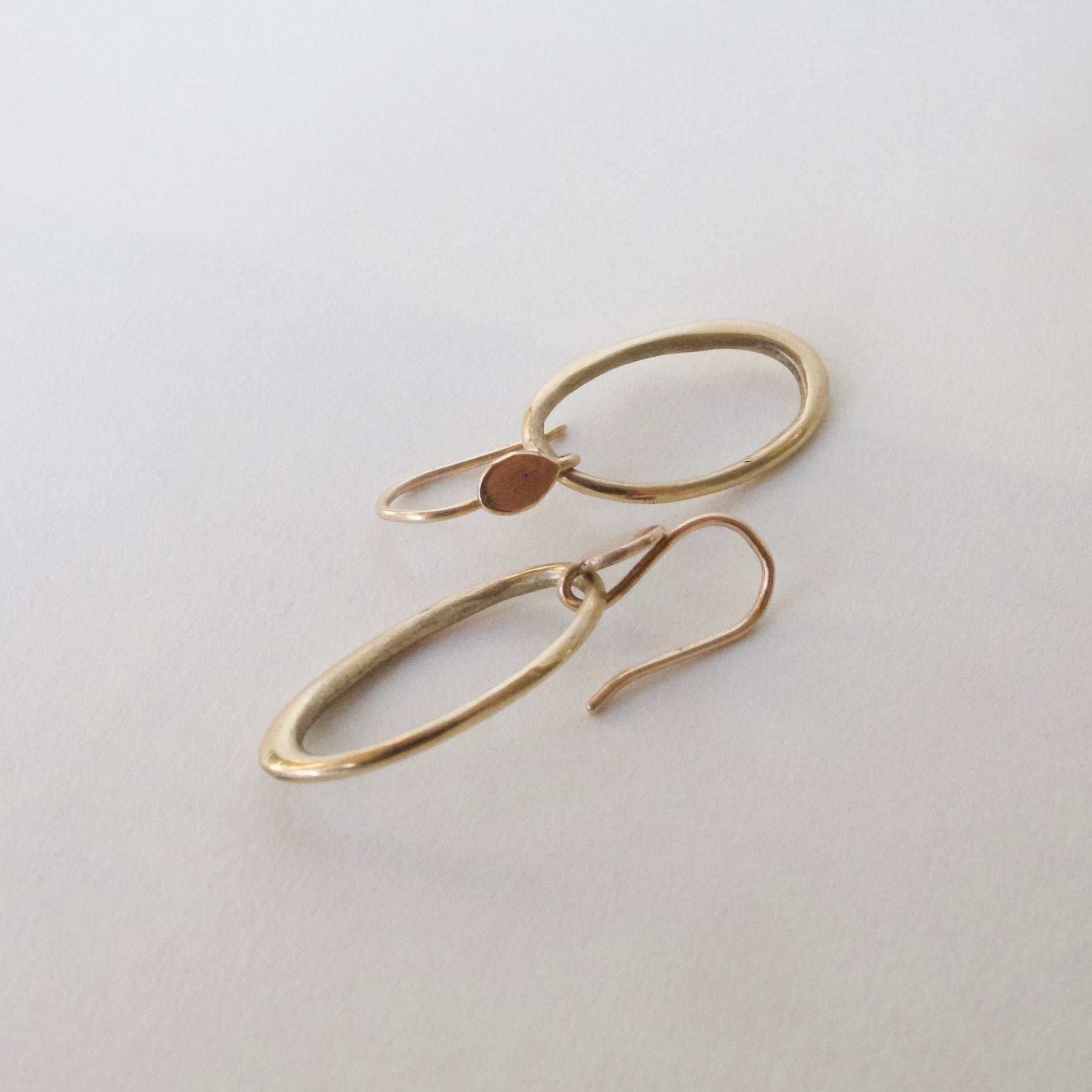 A pair of minimalist, open oval hoop earrings in a warm gold-tone metal, displayed on a clean, light off-white background.