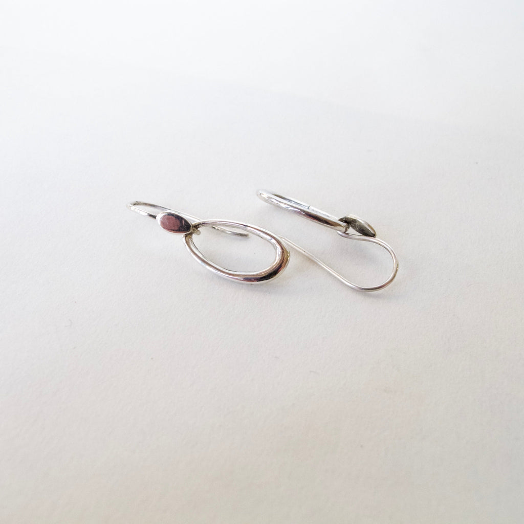 A pair of minimalist silver hoop earrings with leverback closures, displayed on a clean, light off-white background.