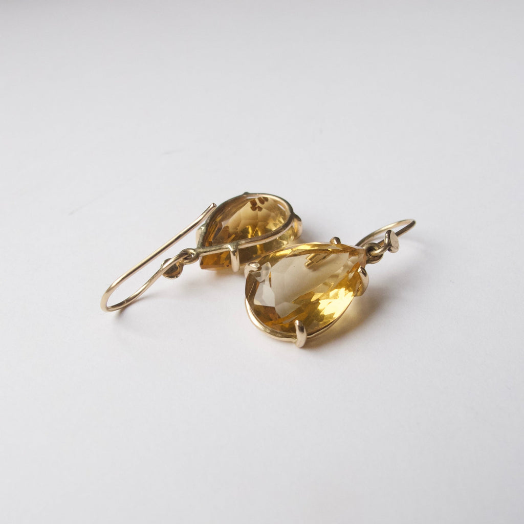 A pair of gold drop earrings featuring large, faceted pear-cut yellow gemstones, displayed on a clean white background.