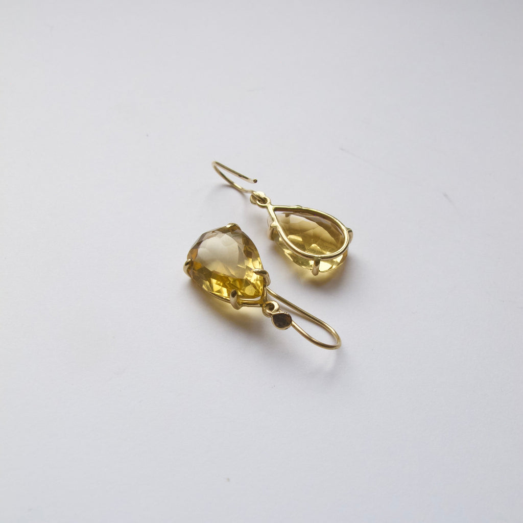 A pair of gold drop earrings with teardrop-shaped yellow gemstones, displayed on a clean white surface.