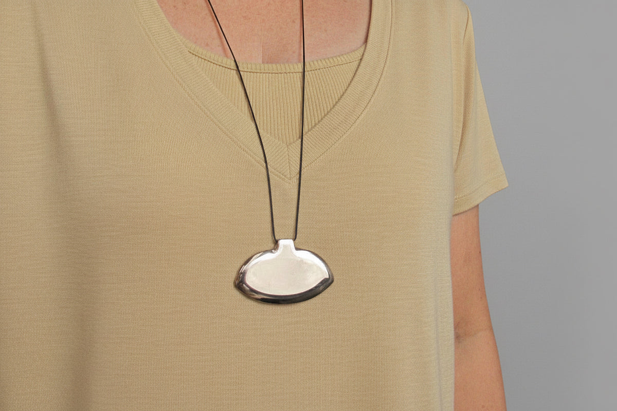 A cropped image of a person in a yellow shirt wearing a smooth polished bronze pendant that is oval and hung horizontally on a thin black cord