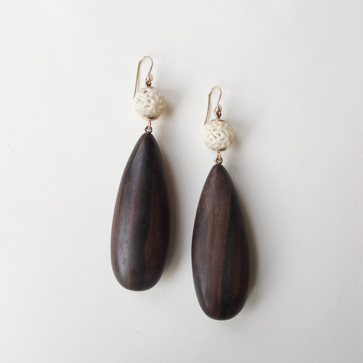A pair of teardrop-shaped dark brown wooden drop earrings with textured cream-colored beads and gold-tone fishhook wires, displayed on a clean off-white background.