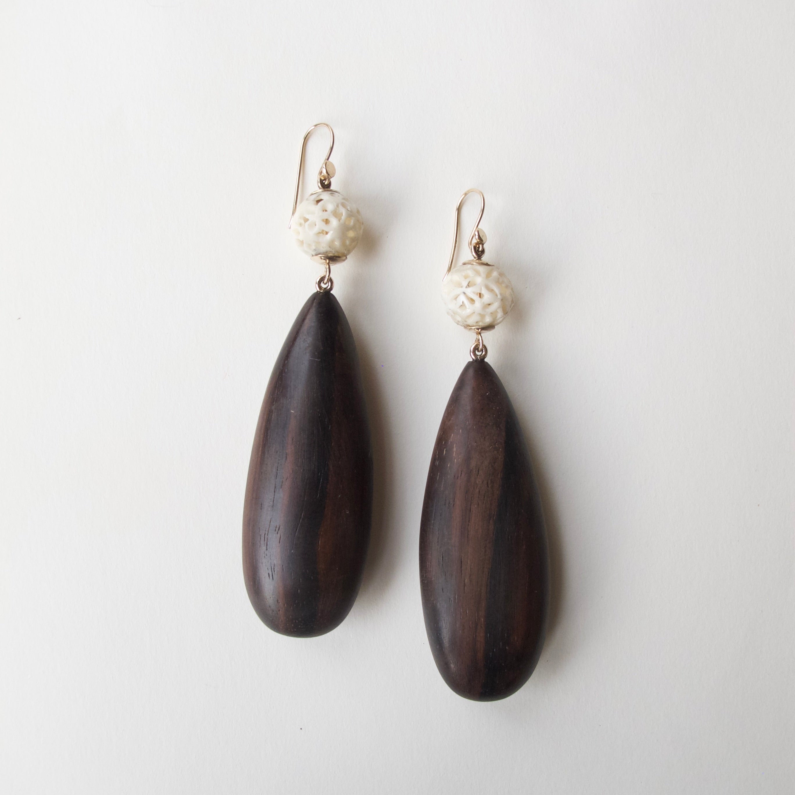 A pair of teardrop-shaped dark brown wooden drop earrings with textured cream-colored beads and gold-tone fishhook wires, displayed on a clean off-white background.