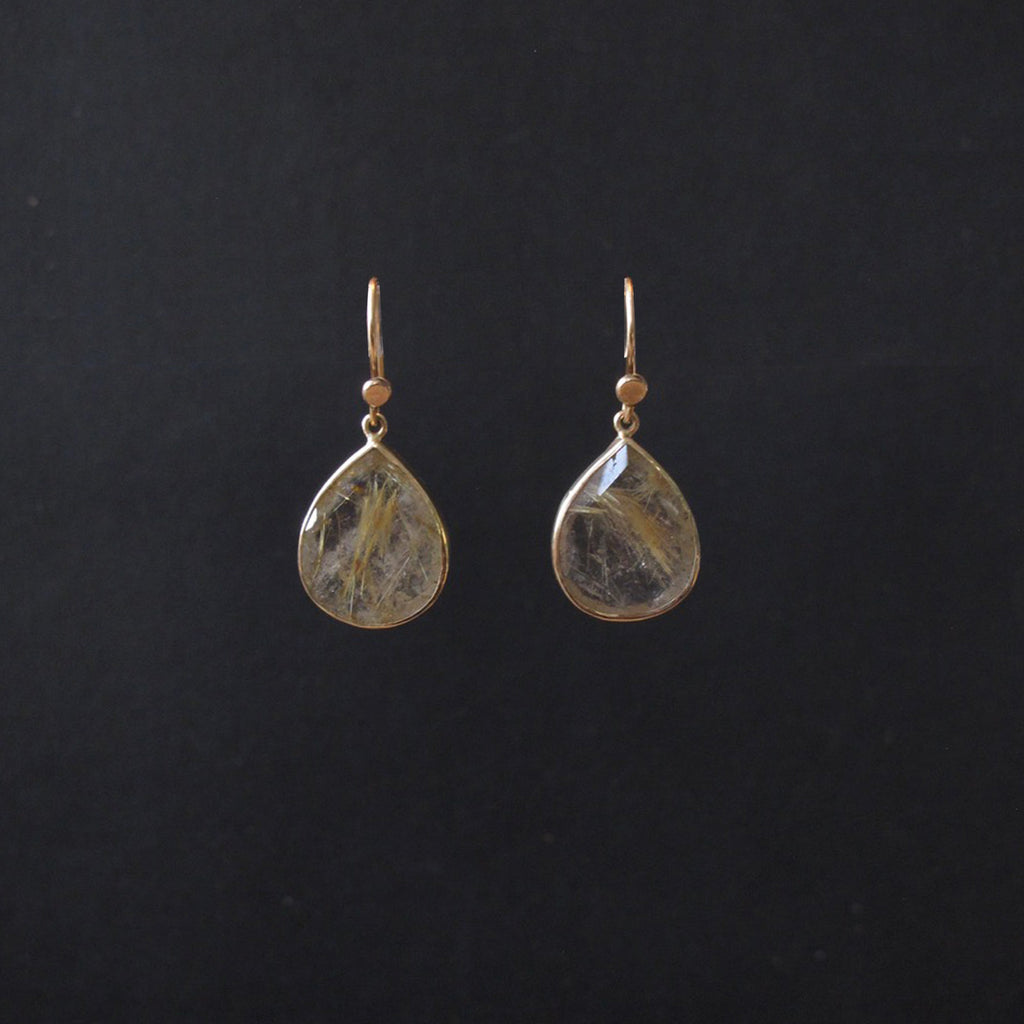 A pair of gold teardrop dangle earrings with clear resin pendants containing fine gold and brown inclusions, displayed against a solid black background.