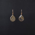 A pair of gold teardrop dangle earrings with clear resin pendants containing fine gold and brown inclusions, displayed against a solid black background.