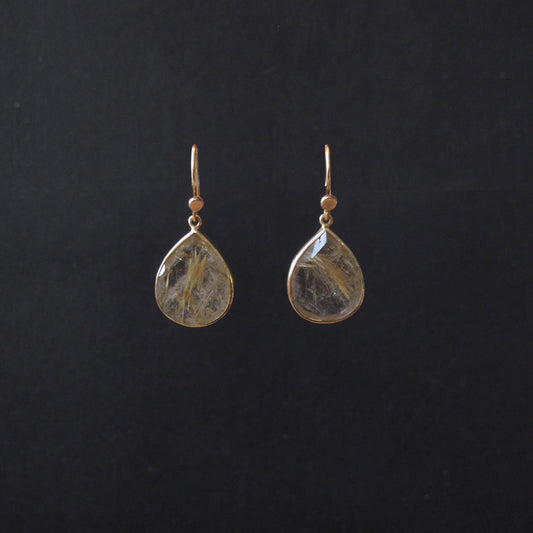 A pair of gold teardrop dangle earrings with clear resin pendants containing fine gold and brown inclusions, displayed against a solid black background.