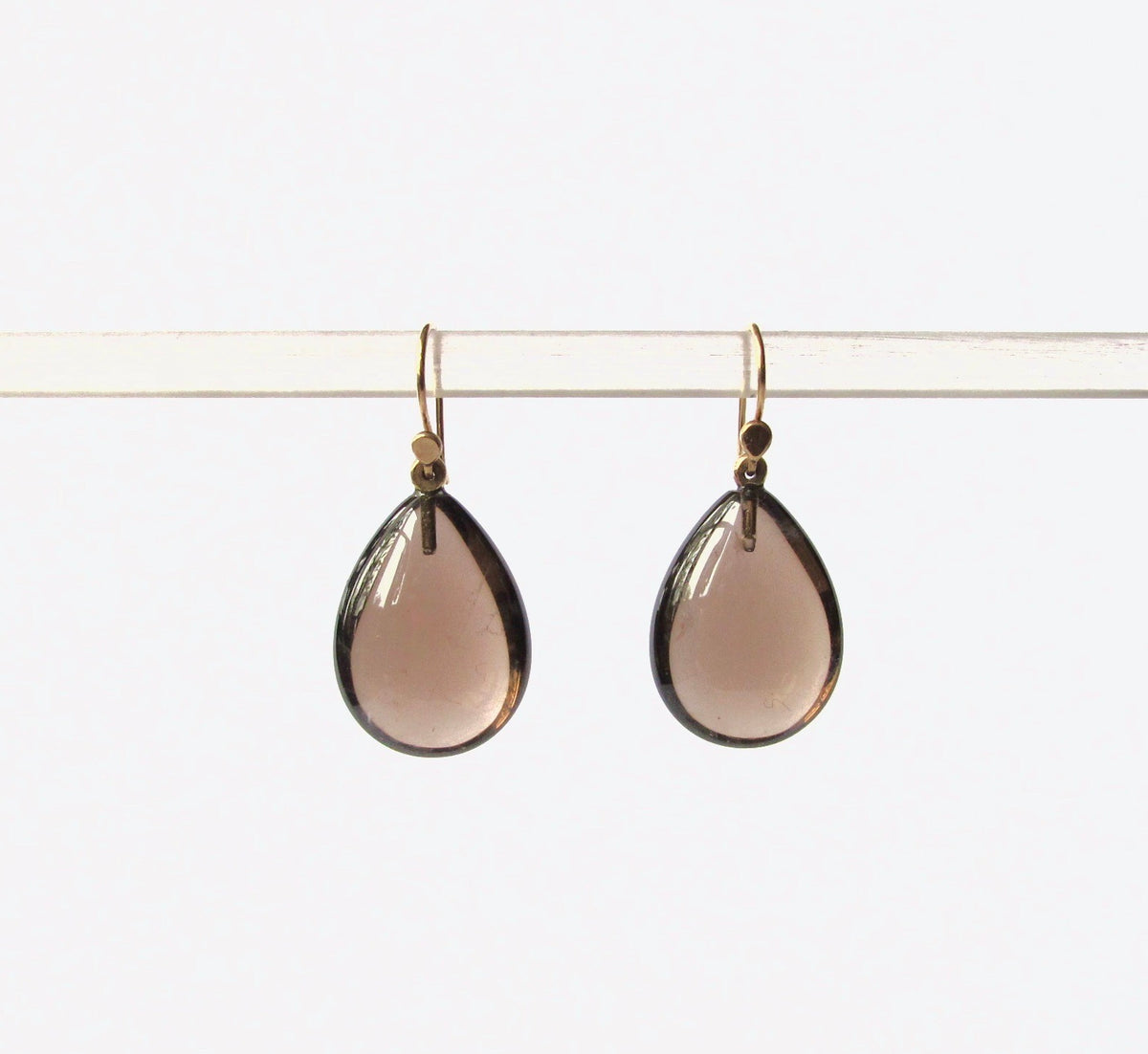 Teardrop-shaped smoky rose gold glass drop earrings hanging from gold-toned fishhook wires on a clear display bar against a white background.