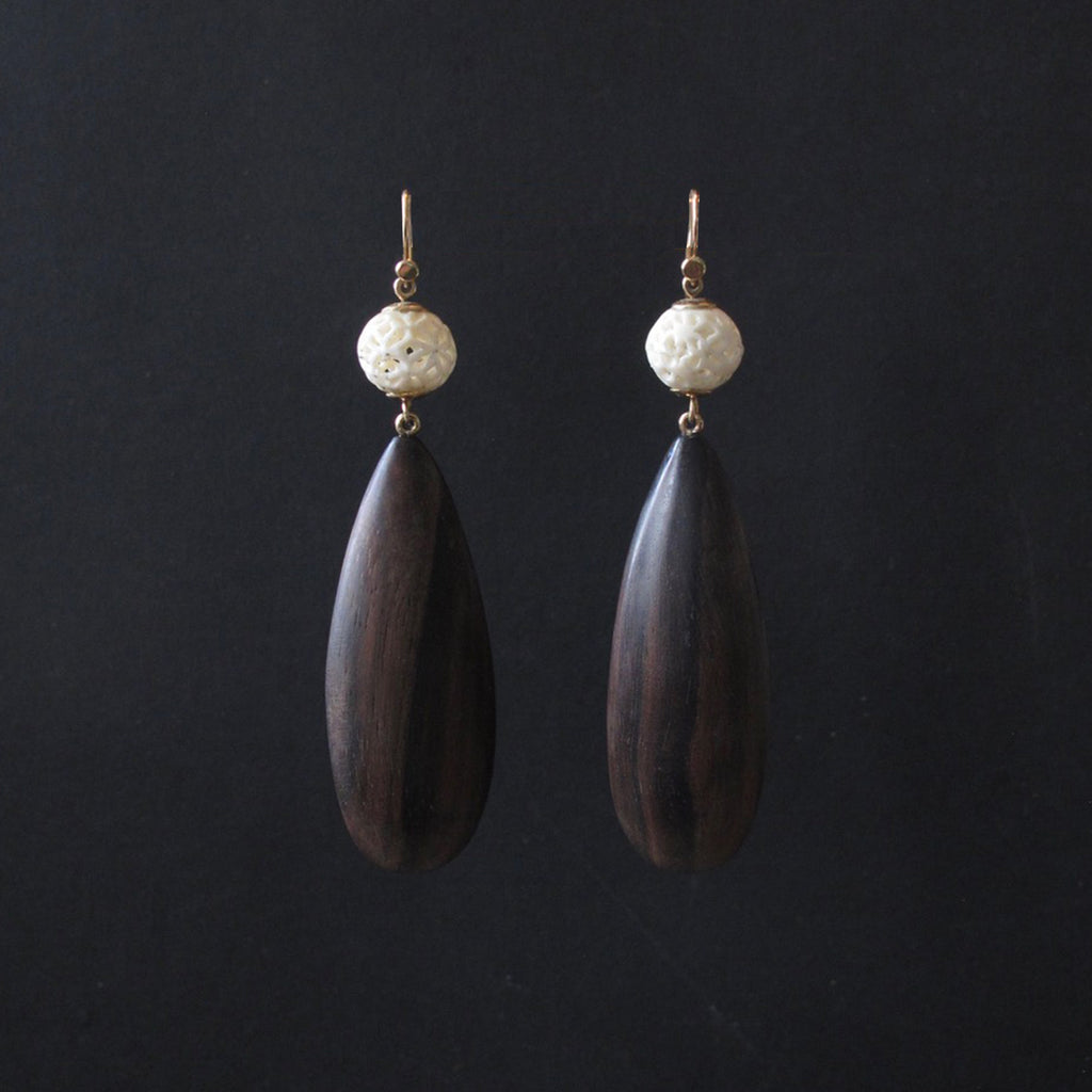 A pair of handmade teardrop dangle earrings featuring dark brown wood pendants, a textured off-white stone bead, and gold-tone hooks, displayed against a solid black background.