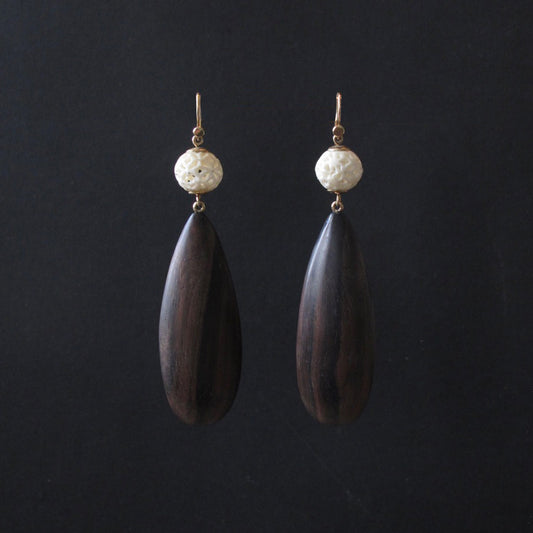 A pair of handmade teardrop dangle earrings featuring dark brown wood pendants, a textured off-white stone bead, and gold-tone hooks, displayed against a solid black background.