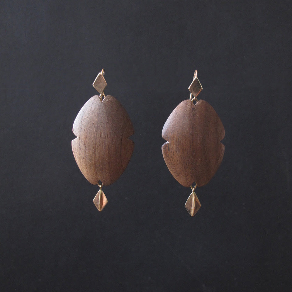 A pair of bohemian-style wooden dangle earrings with a warm medium-brown wood grain and small gold-toned metal accents, displayed against a dark charcoal background.
