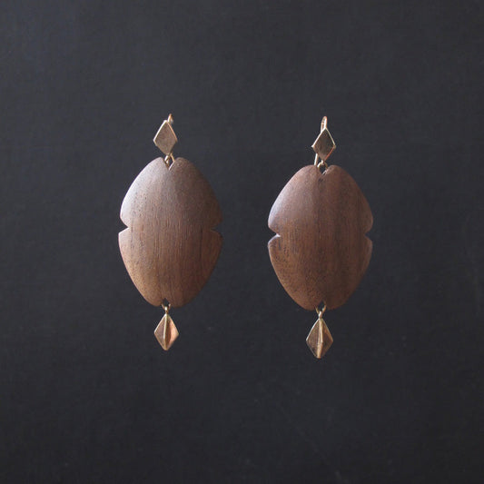 A pair of bohemian-style wooden dangle earrings with a warm medium-brown wood grain and small gold-toned metal accents, displayed against a dark charcoal background.