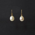 A pair of gold drop earrings with teardrop-shaped white freshwater pearls, displayed against a solid black background.