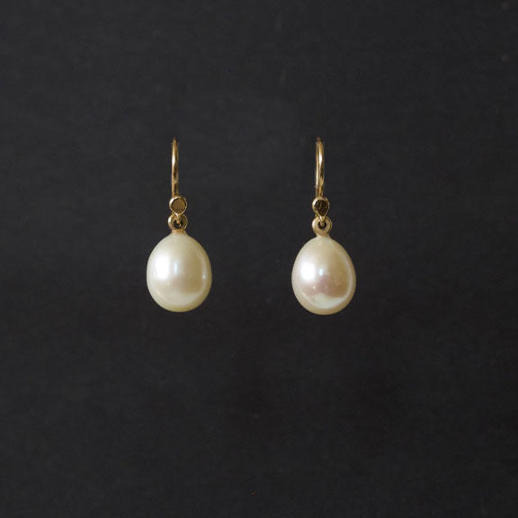 A pair of gold drop earrings with teardrop-shaped white freshwater pearls, displayed against a solid black background.