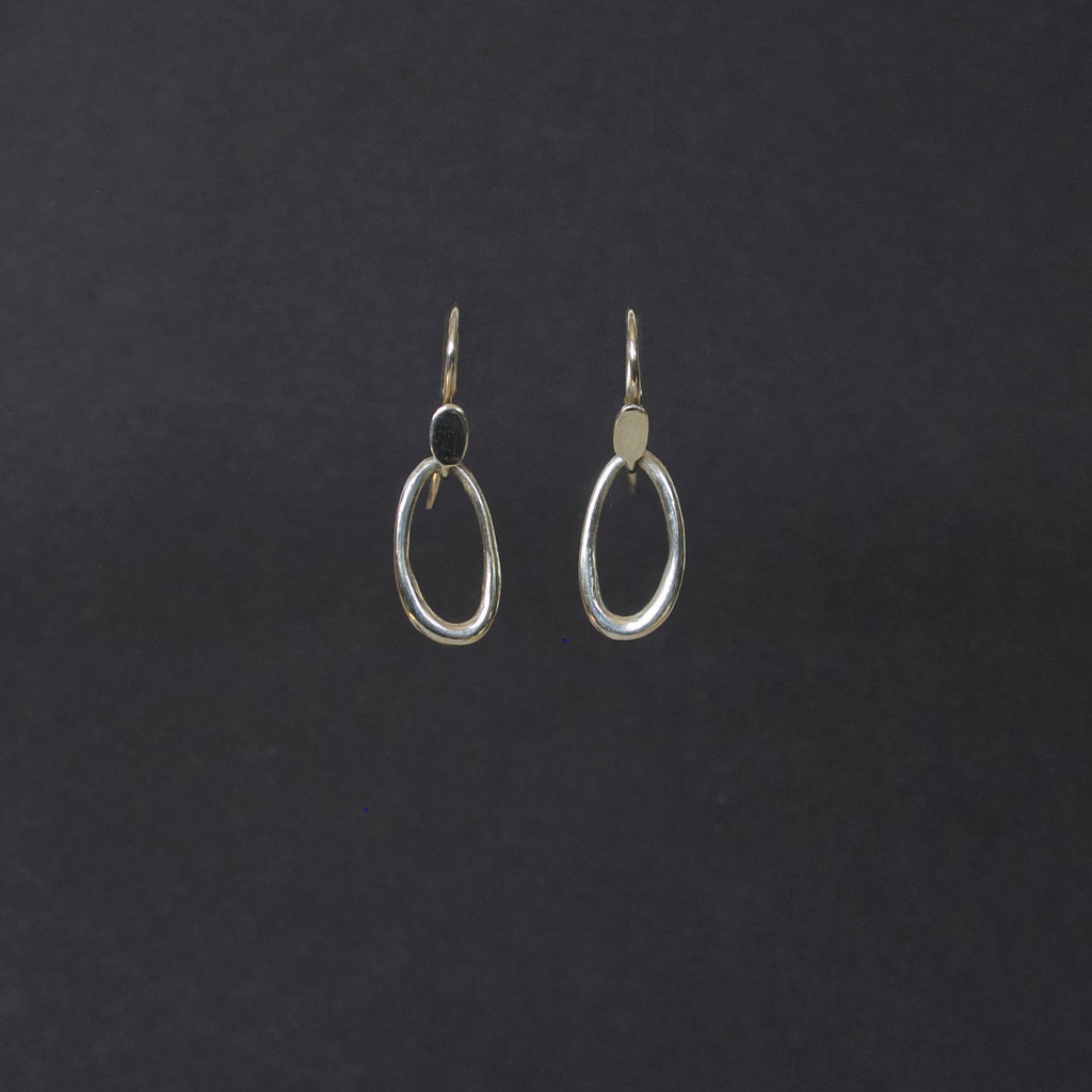 A pair of silver-toned open oval hoop earrings with fishhook backings, displayed against a dark charcoal background.